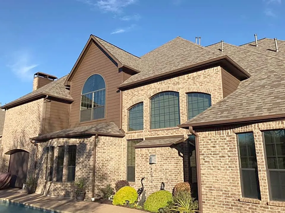 The back of a tan brick two-story with a new shingle roof, beside the pool