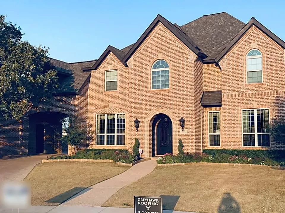 A red brick two-story with a new roof and a GreyHawk Roofing yard sign