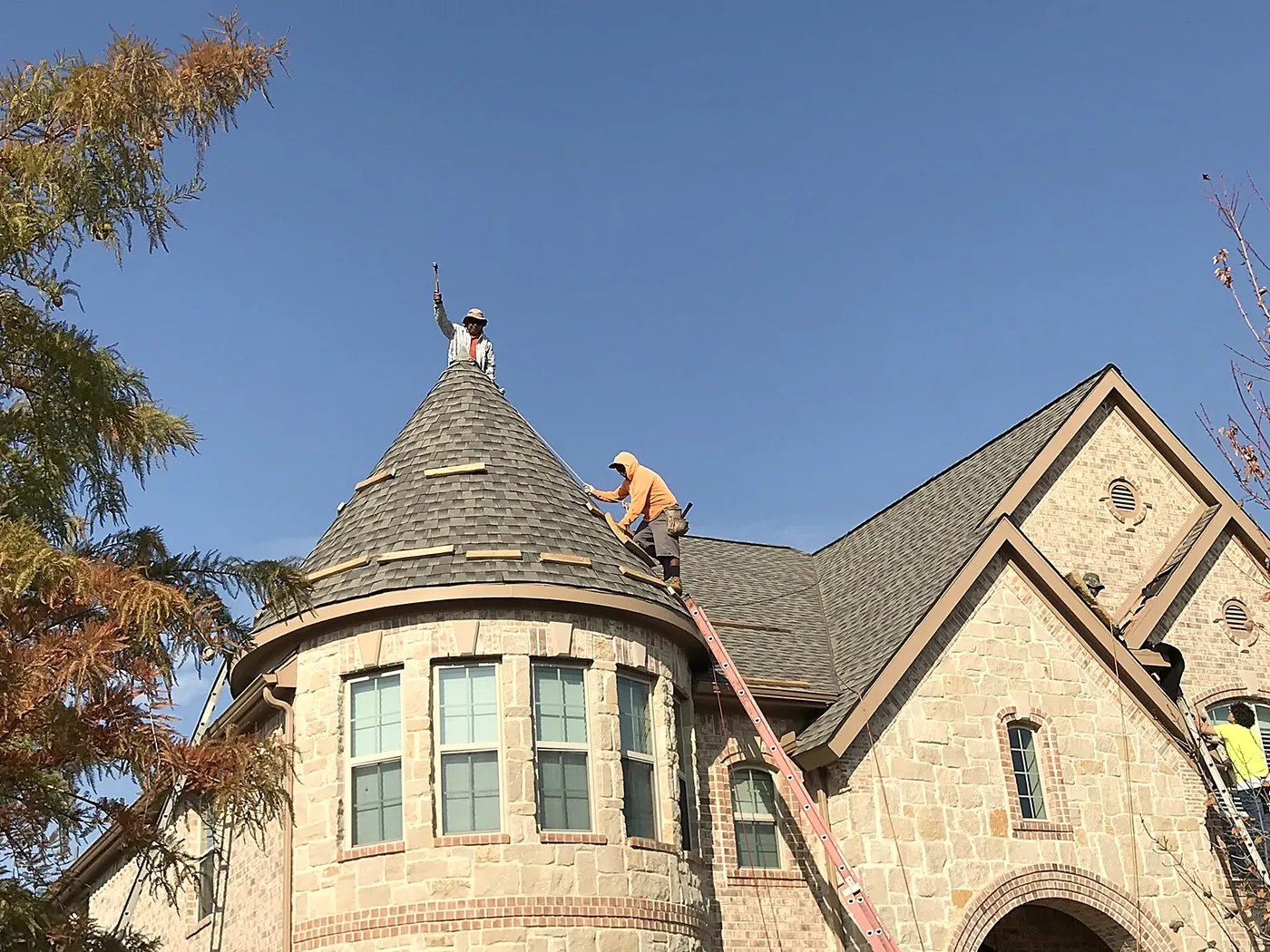 Two GreyHawk roofers shingling a stone turret, one standing at the peak