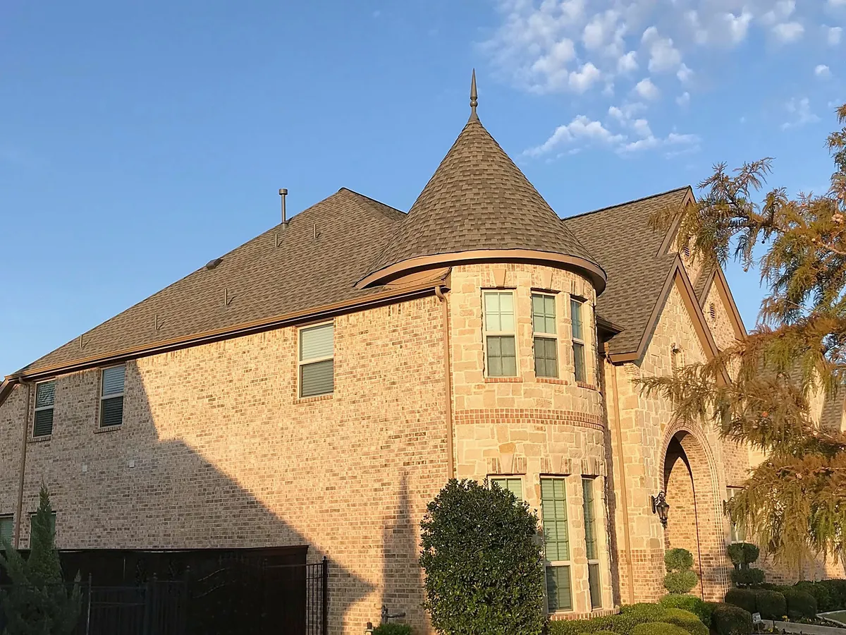 A tan brick home with a round turret under a new brown shingle roof
